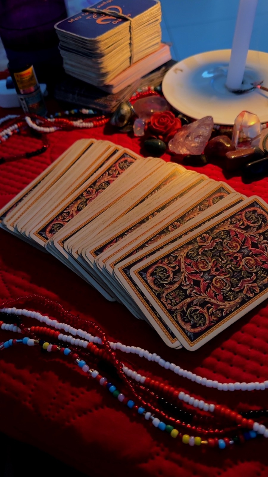 Baralho de tarot aberto em leque sobre manta vermelha, com cristais, uma rosa vermelha e fios de contas coloridas